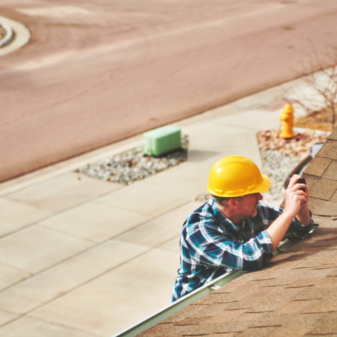 man on top of ladder wearing a hard hat and looking at gutters